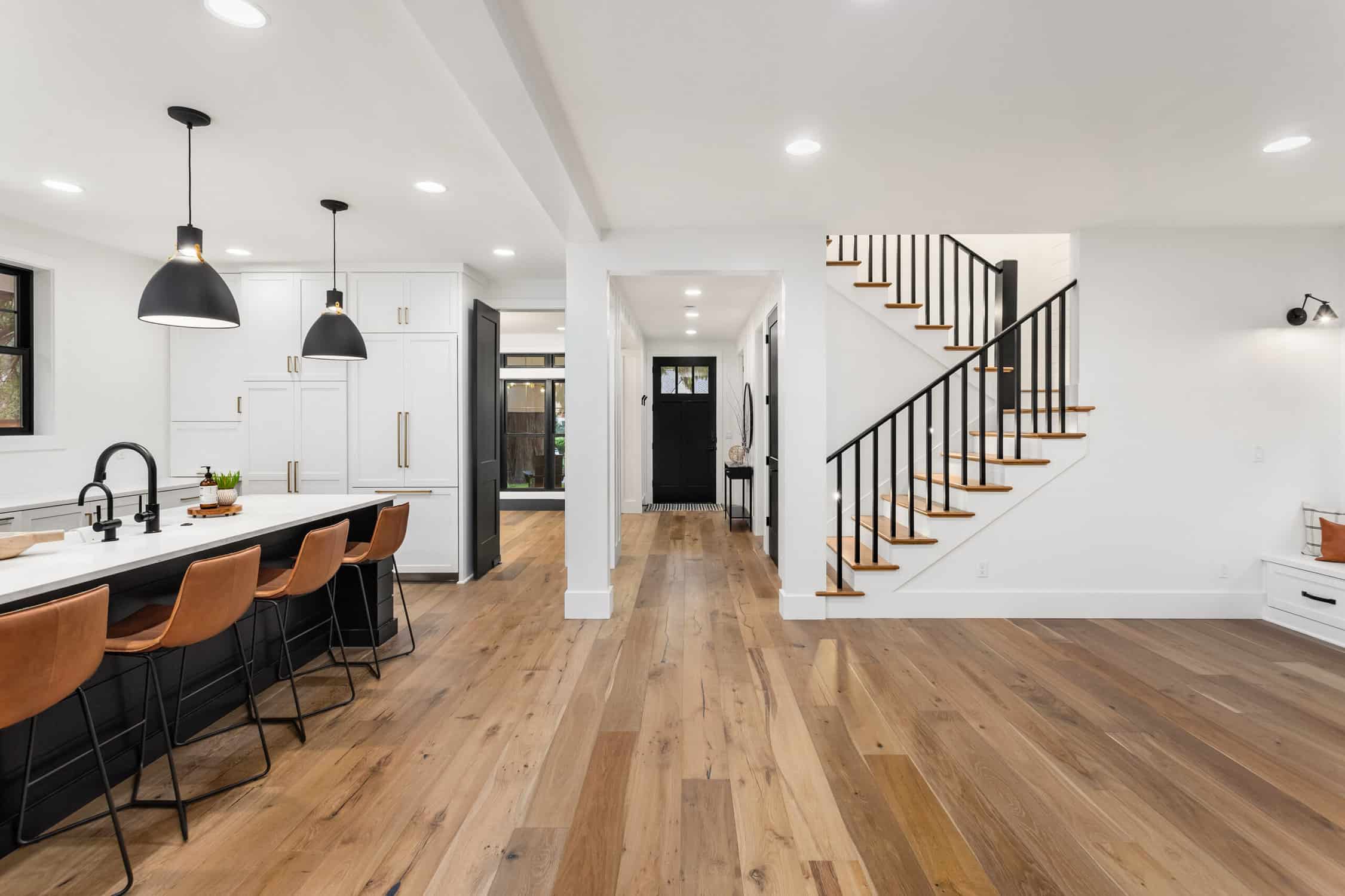 Kitchen and living room interior in new farmhouse style luxury home with open concept floor plan. Features large island with farmhouse sink, hardwood floors, and black accents- remove ceiling water stains